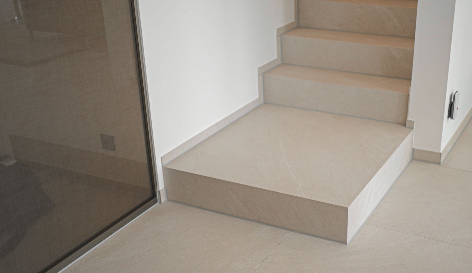 Treppe mit hellen Natursteinstufen hinter einer Glaswand