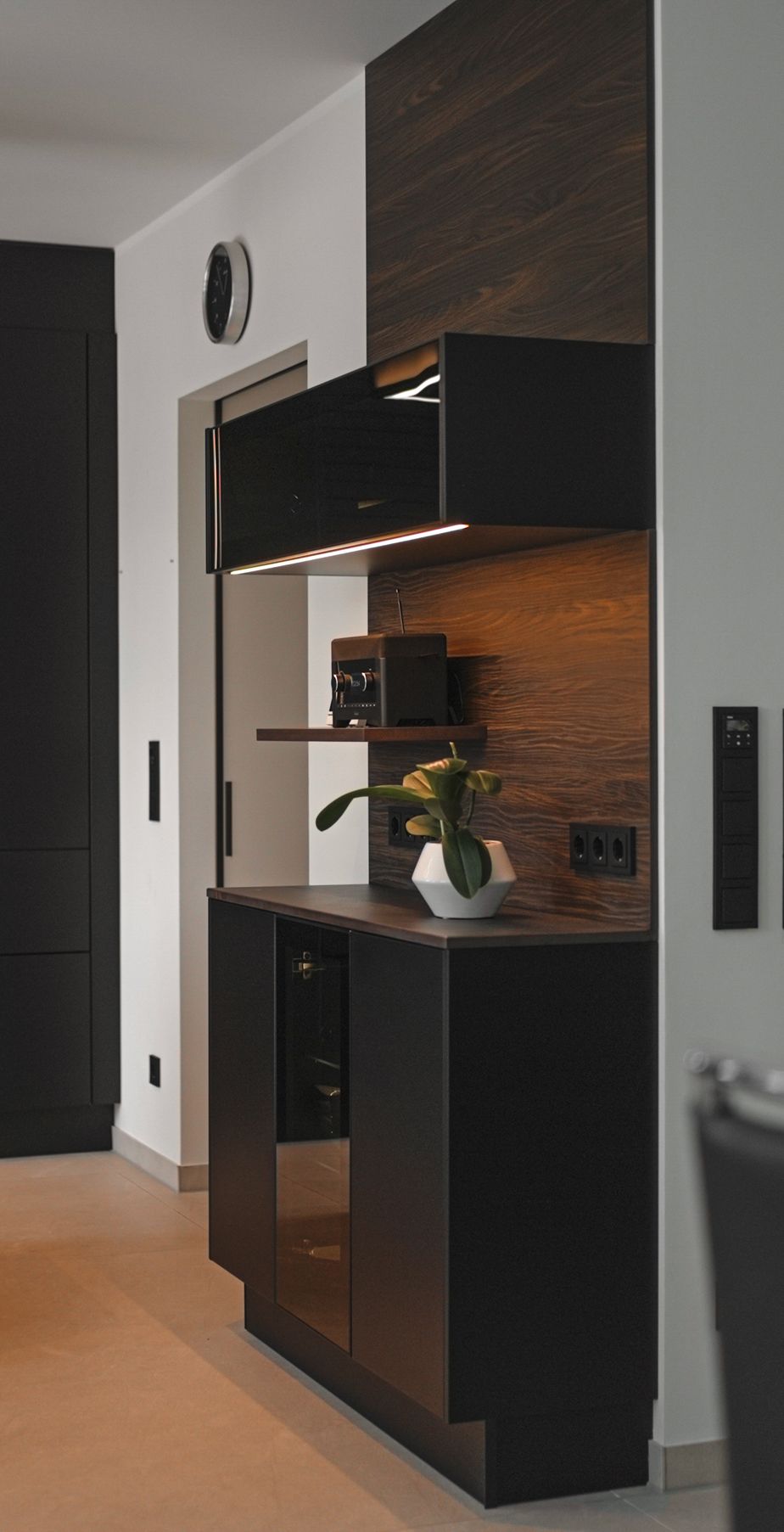 Hochschrank mit Holzrückwand und beleuchteter Nische in einer dunklen Küche