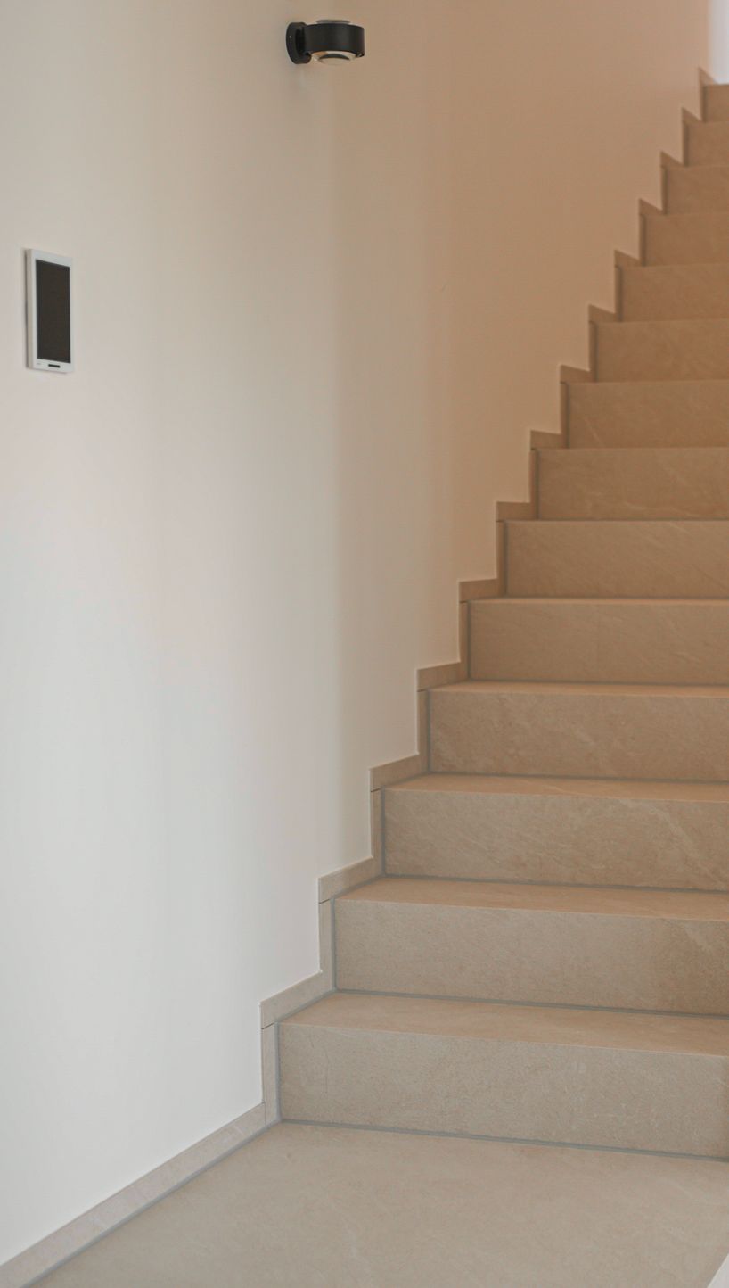 Treppe mit hellen Natursteinstufen entlang einer weißen Wand