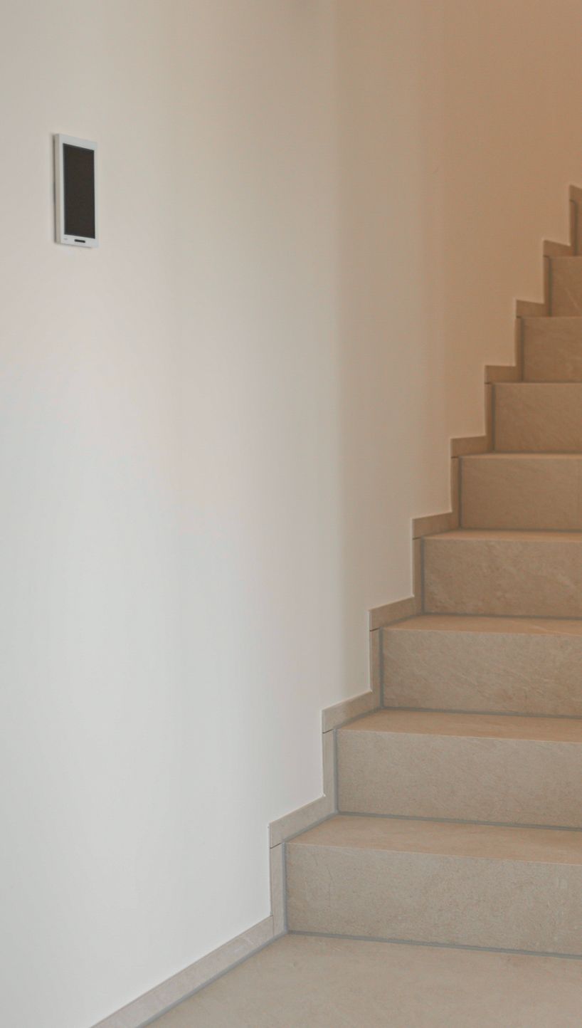Treppe mit hellen Natursteinstufen entlang einer weißen Wand
